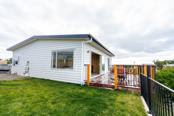 Photo of exterior of renovated bach showing new hardwood deck, railing and exterior weatherboard cladding