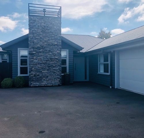 Photo of exterior of new build designed and built by Code Construction Canterbury. Feature schist chimney and new fence