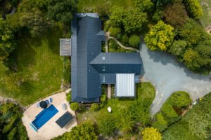 Aerial drone photo of renovation project by Code Construction. Shows birds eye view of house with new roof including garage and louvre system with decking and pool area