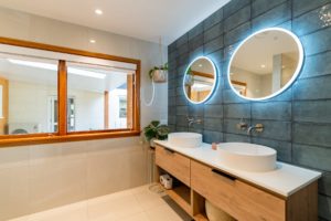 New bathroom renovation completed by Code Construction. Shows double sinks, two LED mirrors and beautiful large blue tiles